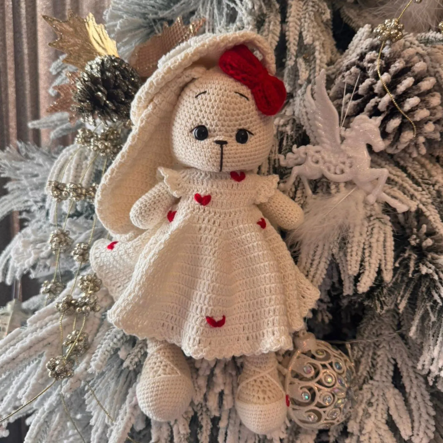 Lepurushe kremi me fjongo të kuqe mes degëve të një peme festive